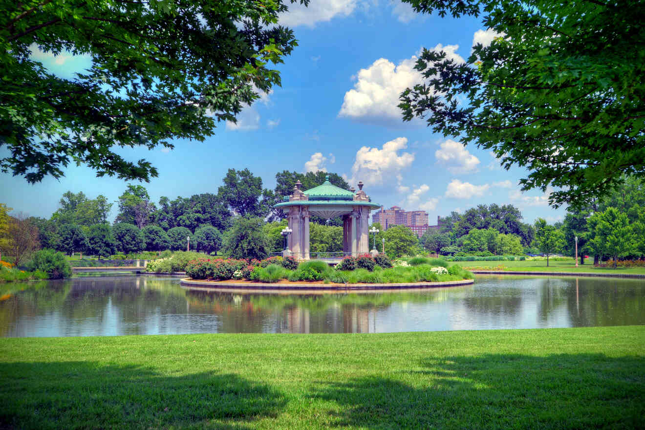 A serene park scene with a large gazebo by a pond surrounded by lush greenery and vibrant flower beds under a clear sky